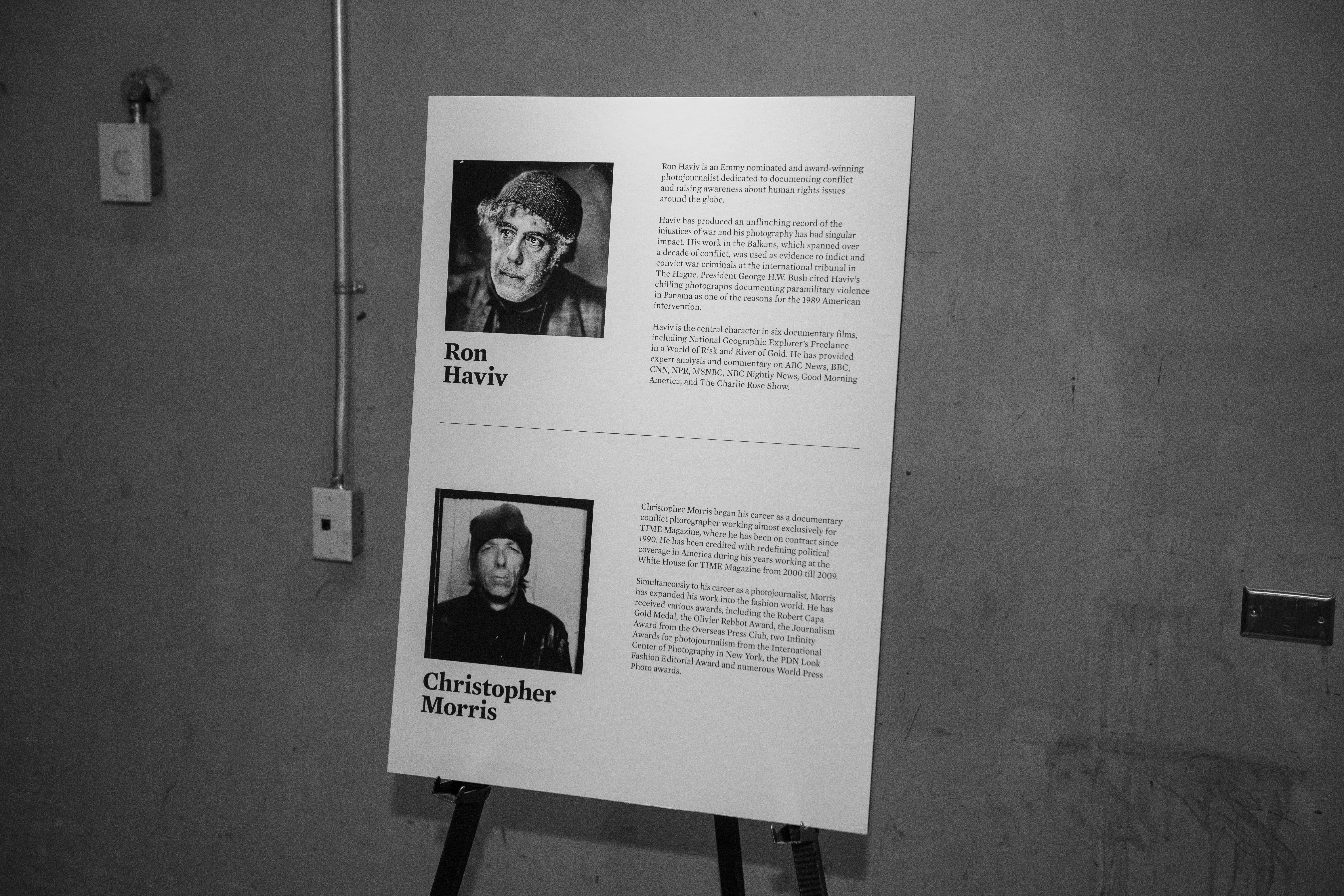 A board on an easel with information about Ron Haviv's and Christopher Morris' life work as photojournalists.