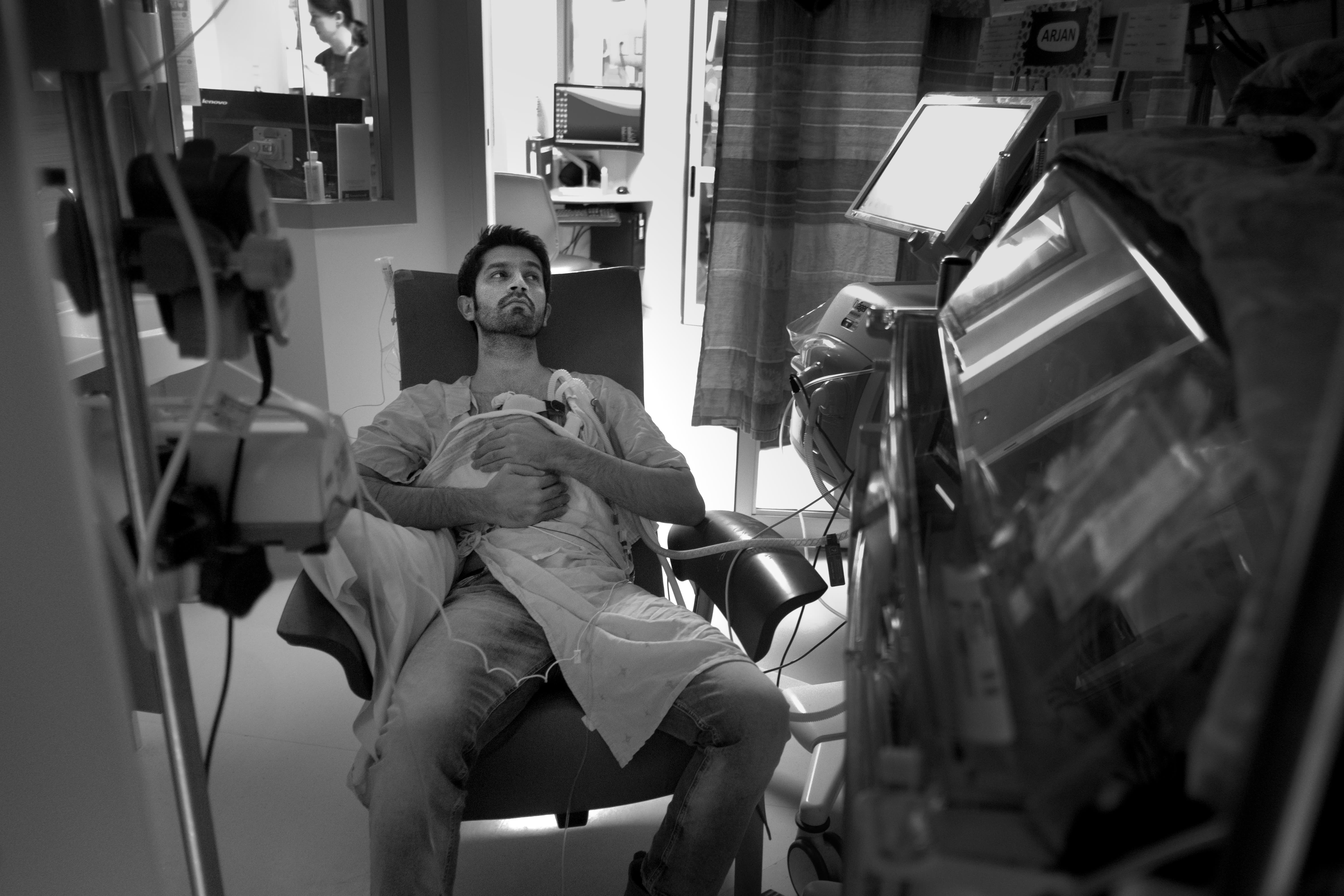 A man holding a baby against his chest. The baby is attached to machines by tubes.