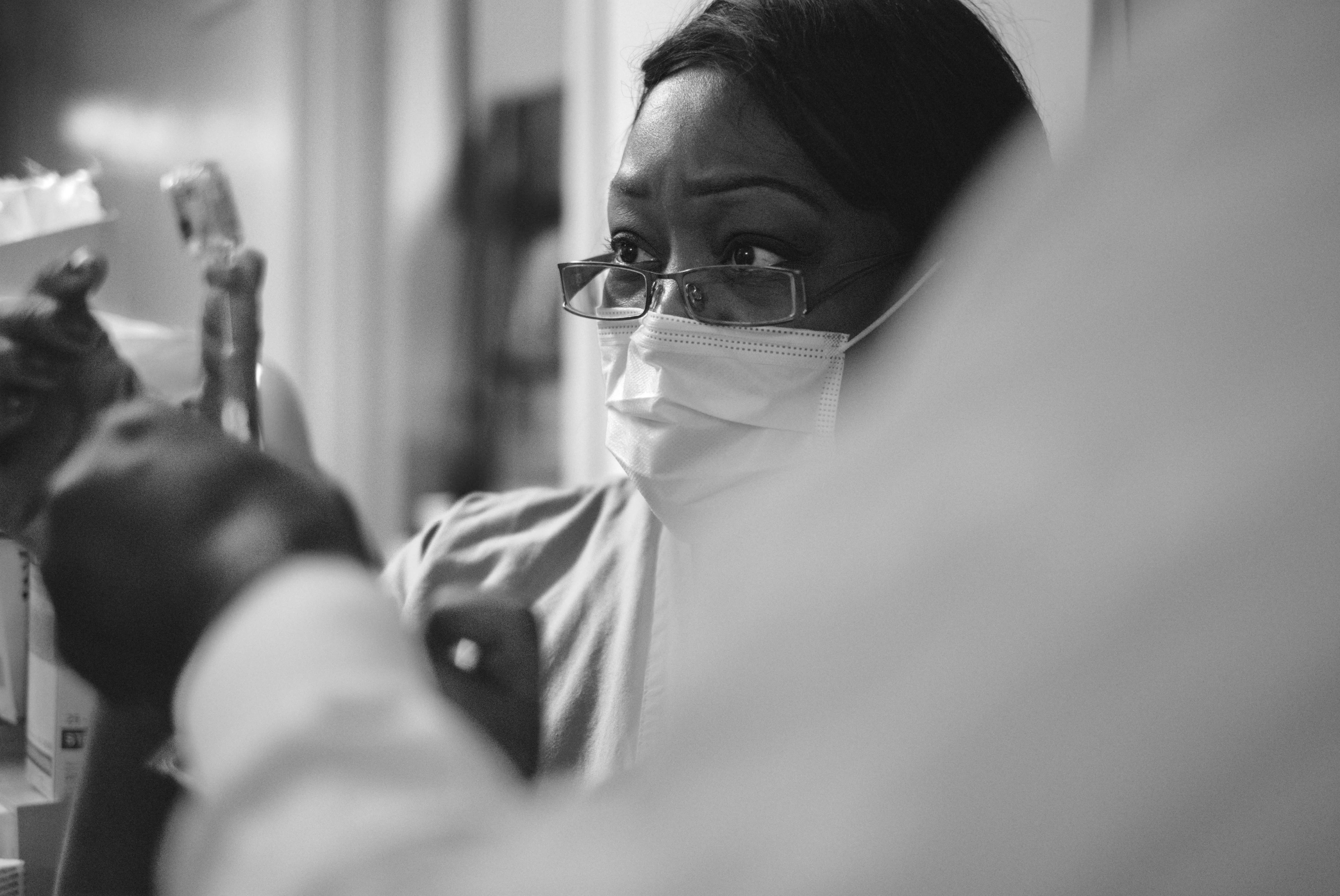 A doctor wearing glasses and a surgical mask looking at something a nurse is showing her.