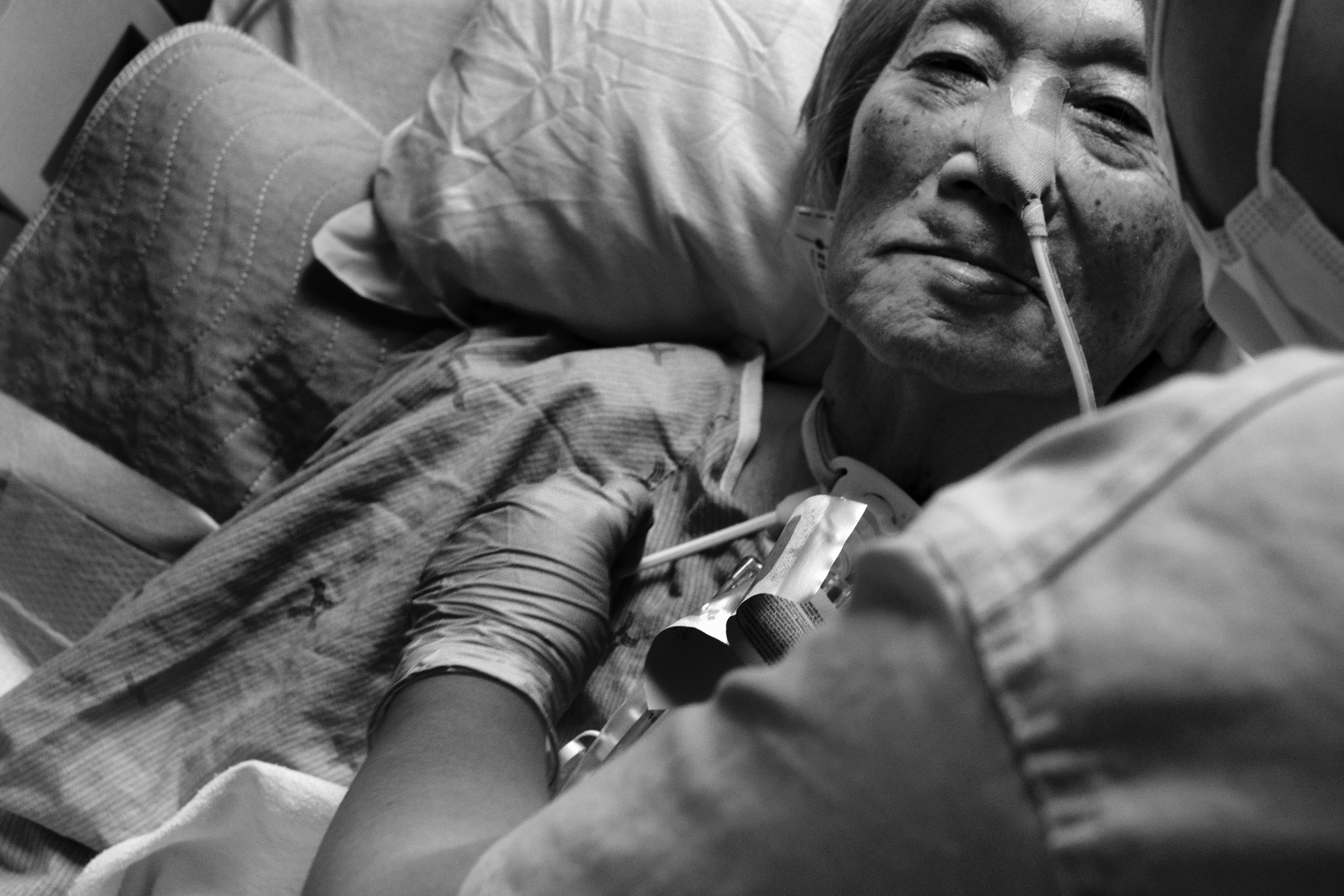 An elderly patient lying down with a tube attached to her nose being looked after by a nurse.